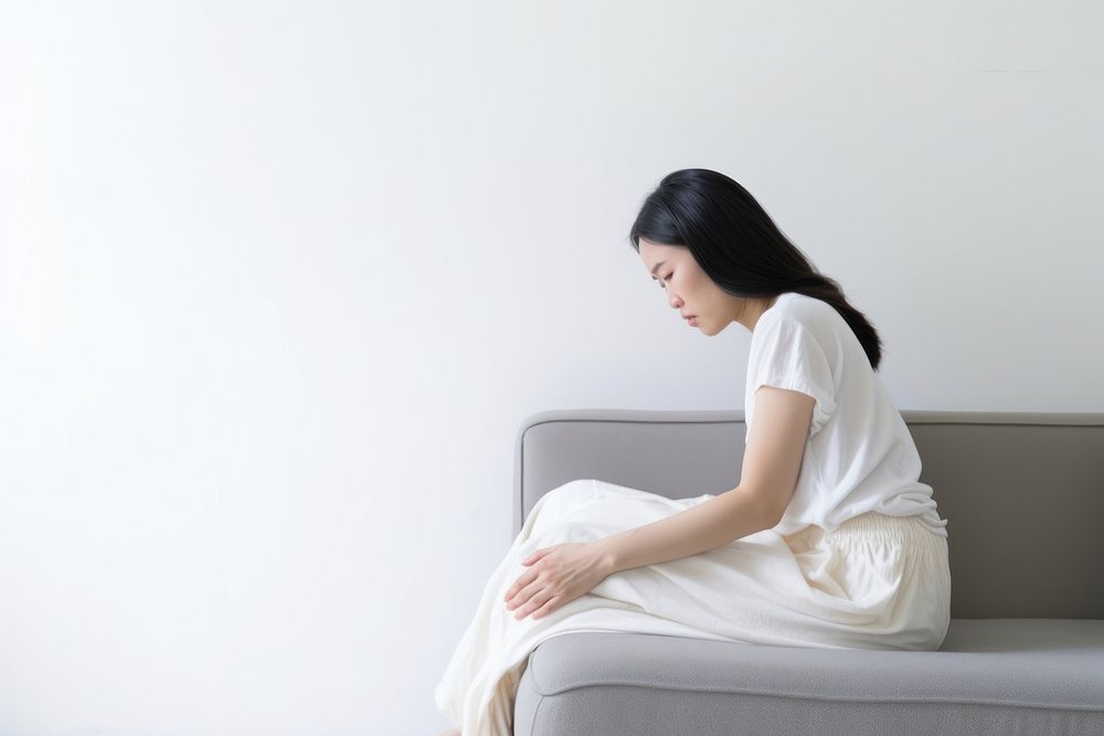 An east asian woman suffering from sickness sitting sofa contemplation.
