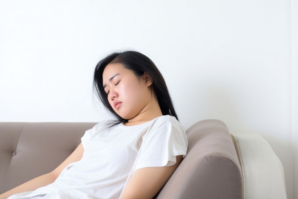 An east asian woman suffering from sickness sleeping sitting sofa.