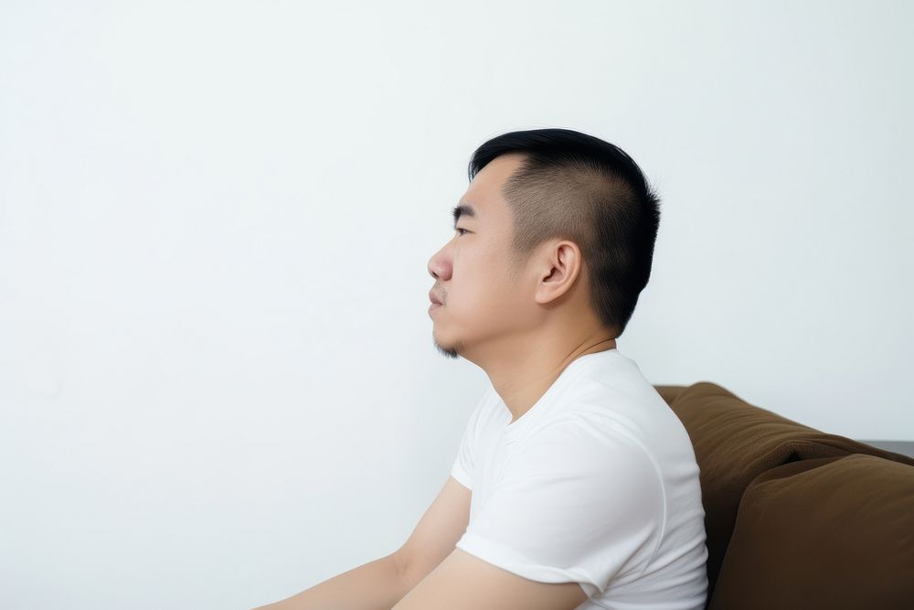 An east asian man suffering from sickness sitting sofa contemplation.