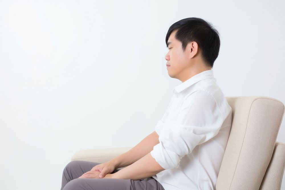 An east asian man suffering from sickness sitting sofa contemplation.