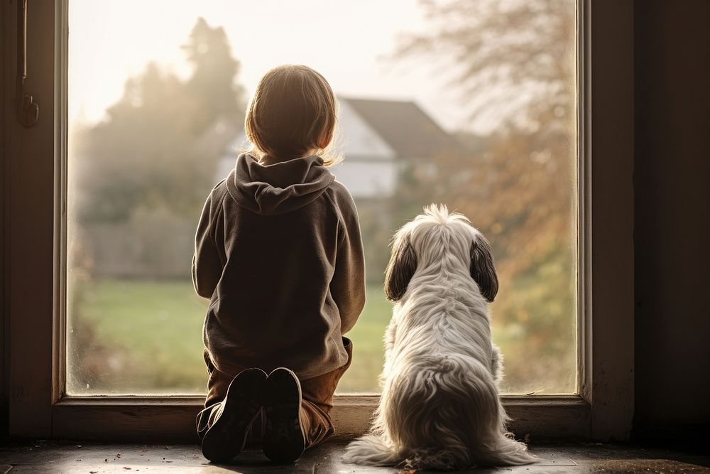 A child and a dog stood looking out the window sitting mammal animal.