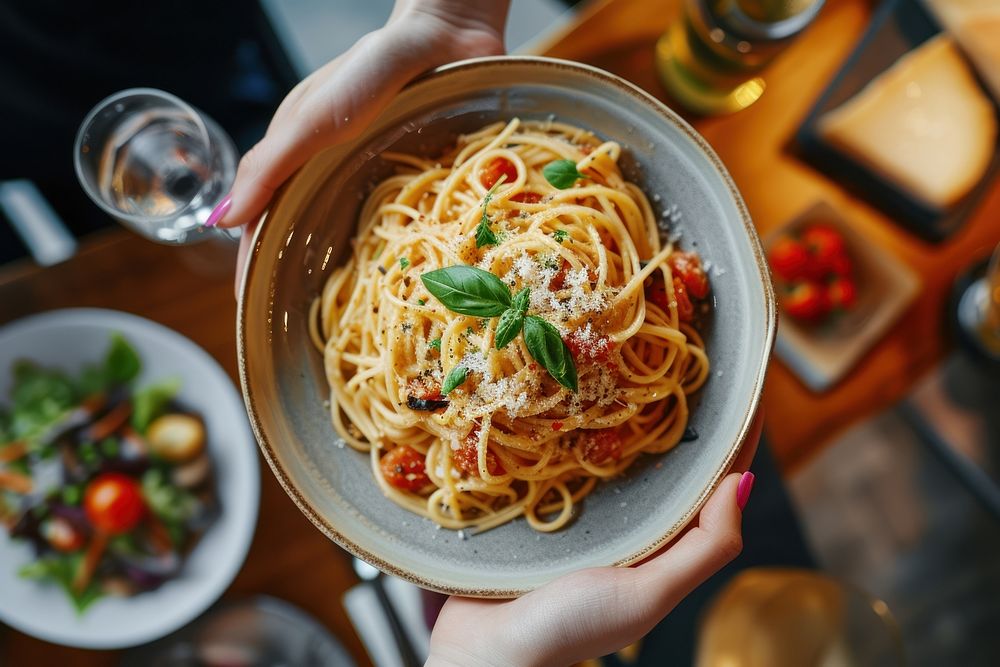 Hands holding pasta dish restaurant spaghetti plate.