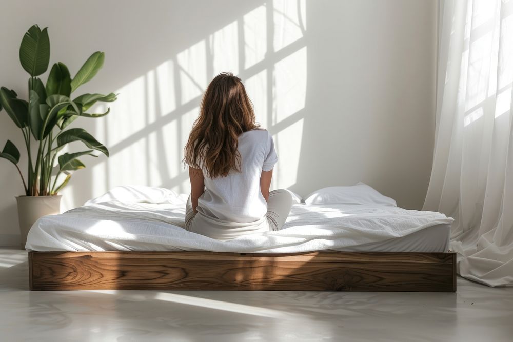 Woman is sitting on the floor in bed furniture mattress sheet.