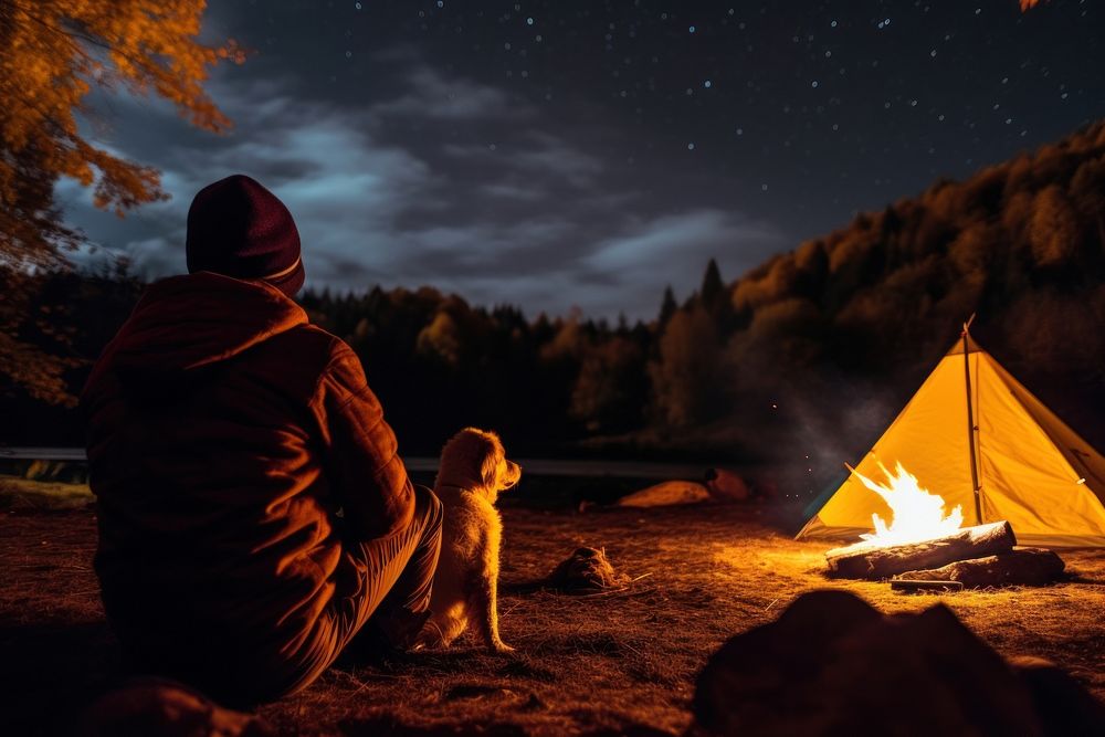 Young alone people and their pets camping in autumn night outdoors bonfire.