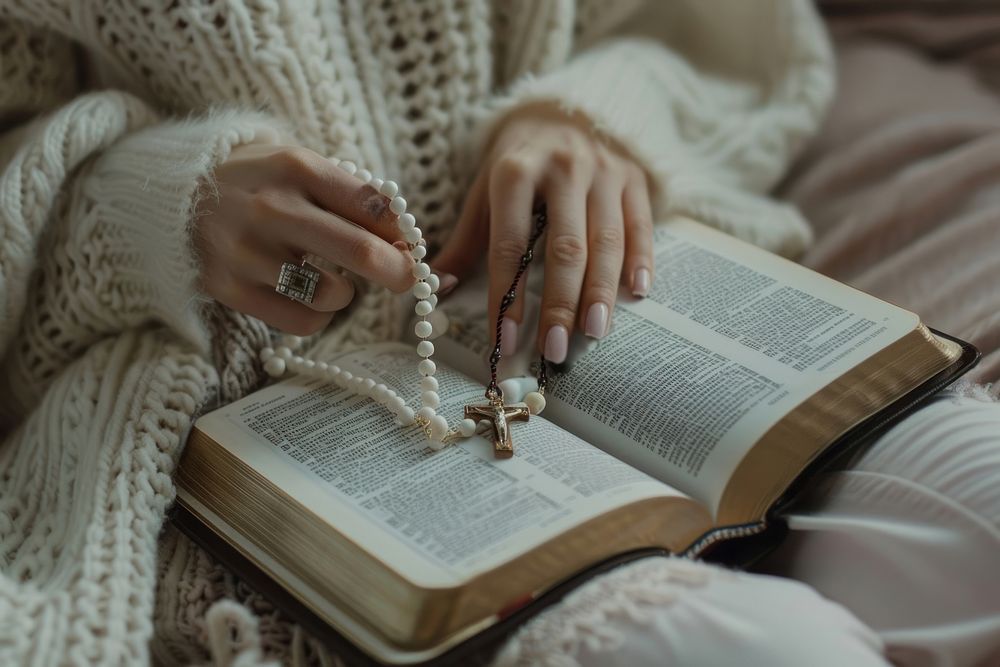 Woman hand holding rosary over bible publication jewelry book.