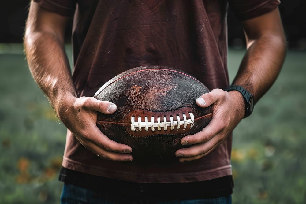 A man holding a football ball sports midsection standing.