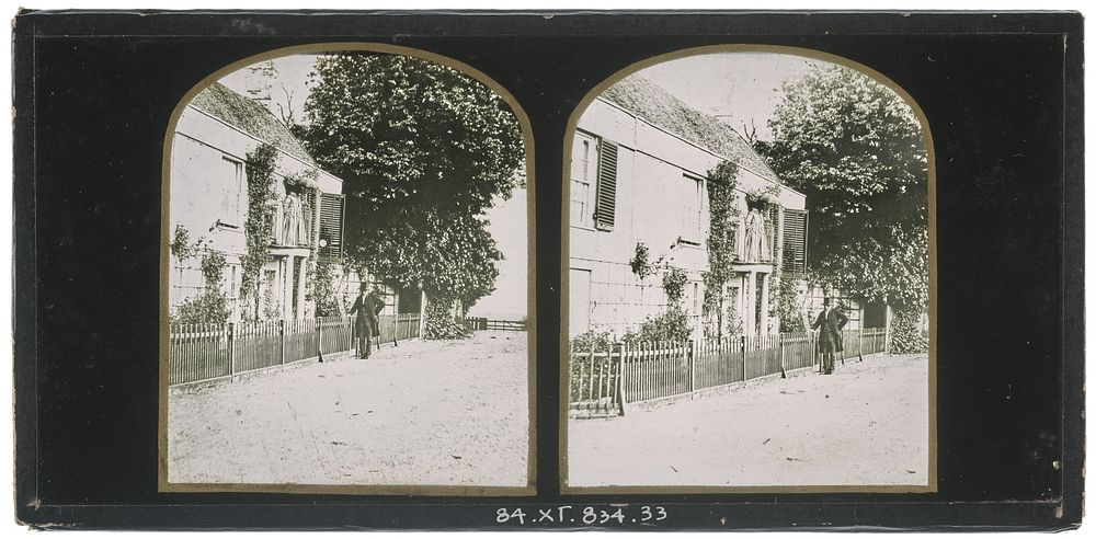 Unidentified British man wearing a top hat standing outside a two-storey house, an unidentified woman standing on the second…