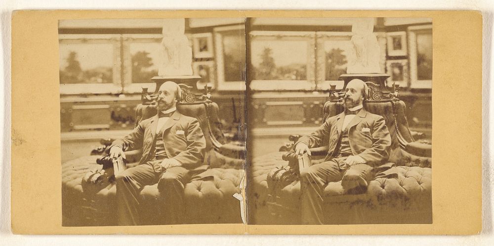 Close-up of bearded, bald gentleman seated on circular couch in his private art gallery, holding a carte-de-visite album