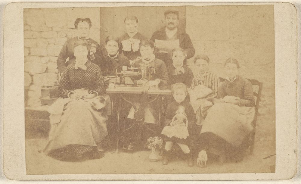 Group of ten men, women, and children sitting around a sewing machine