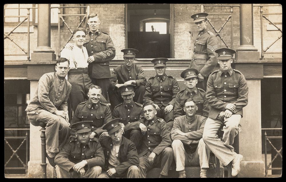 Soldiers posing for a group portrait outside a large building. Photographic postcard, 191-.