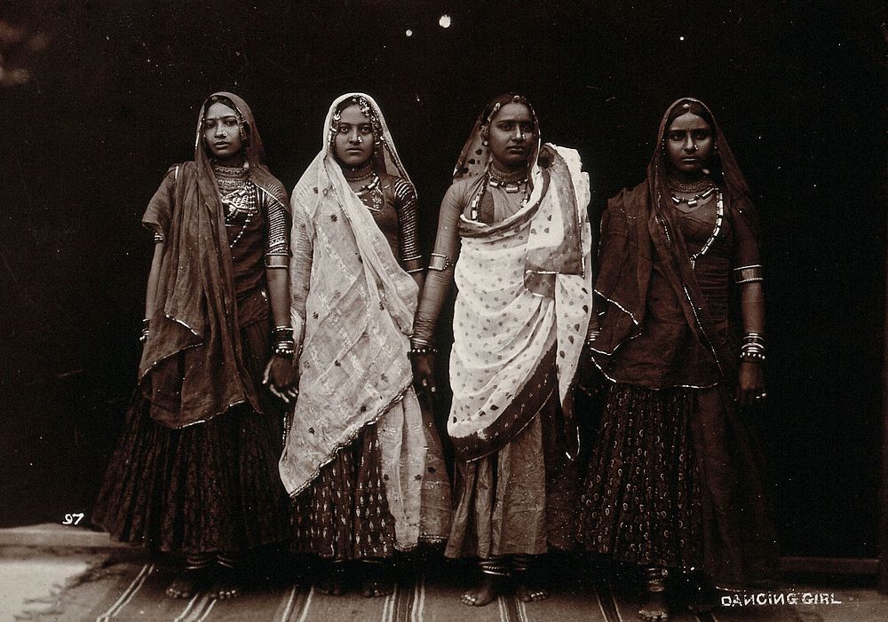 A troupe of nautch dancing girls, standing in a line holding hands, in a studio setting. Photograph, ca.1900.