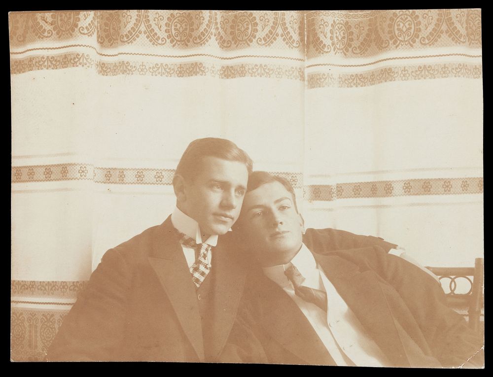 Two men resting close to one another, wearing formal attire. Photograph, 1910.
