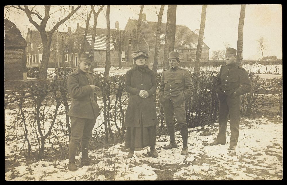 Four Dutch servicemen, one in drag, standing on snowy ground near residential property. Photographic postcard, ca. 1910.