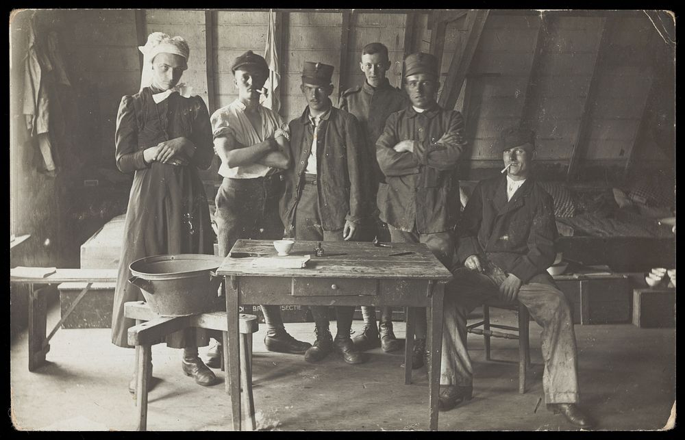 French prisoners of war, one in drag, gather round a small wooden table. Photographic postcard, 191-.