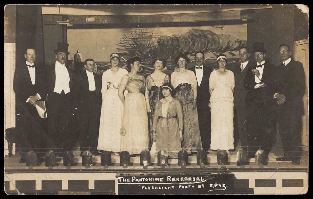 Amateur actors, some in drag, posing on stage for a group portrait. Photographic postcard by E. Pye, 191-.