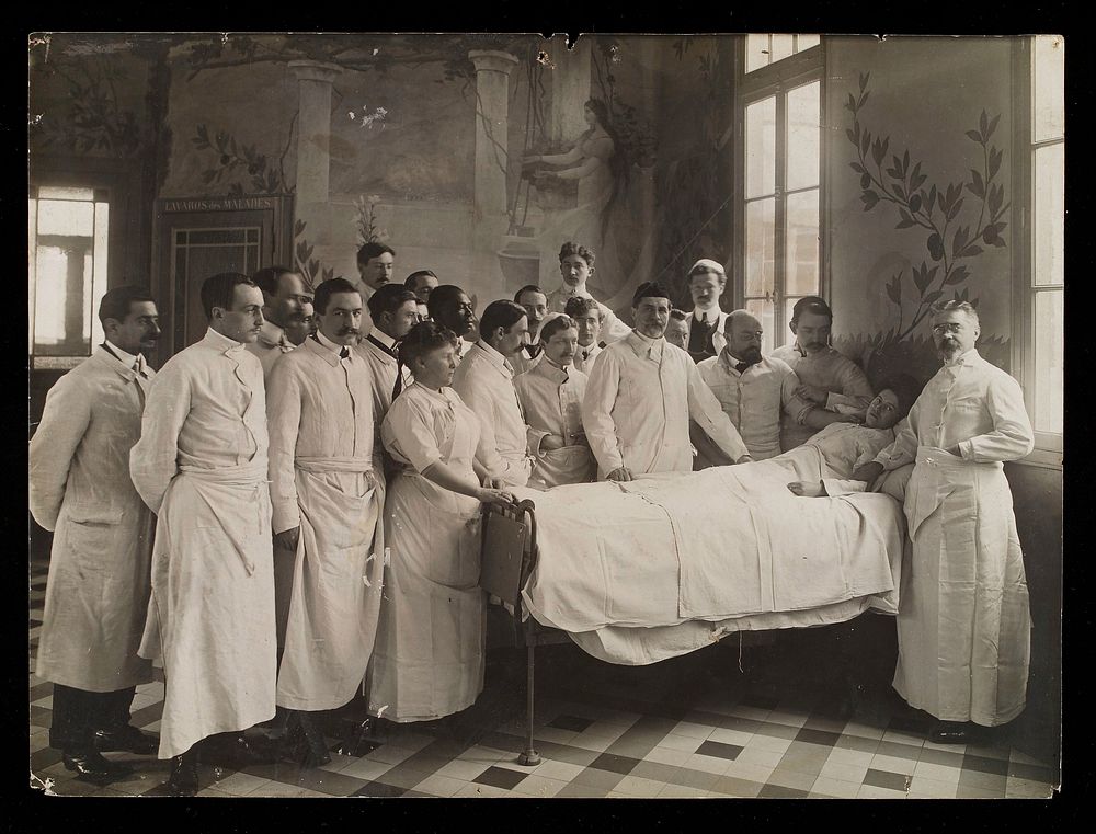 Medical staff standing round a woman patient in bed in a hospital ward. Photograph by Seeberger Frères, ca. 1910.