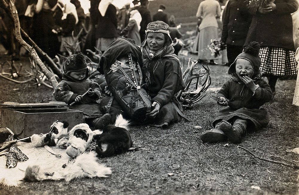 A Lapp (Sami) woman holding her baby in a child carrier, her two toddlers beside her. Photograph by Davey & Hackney, ca.…