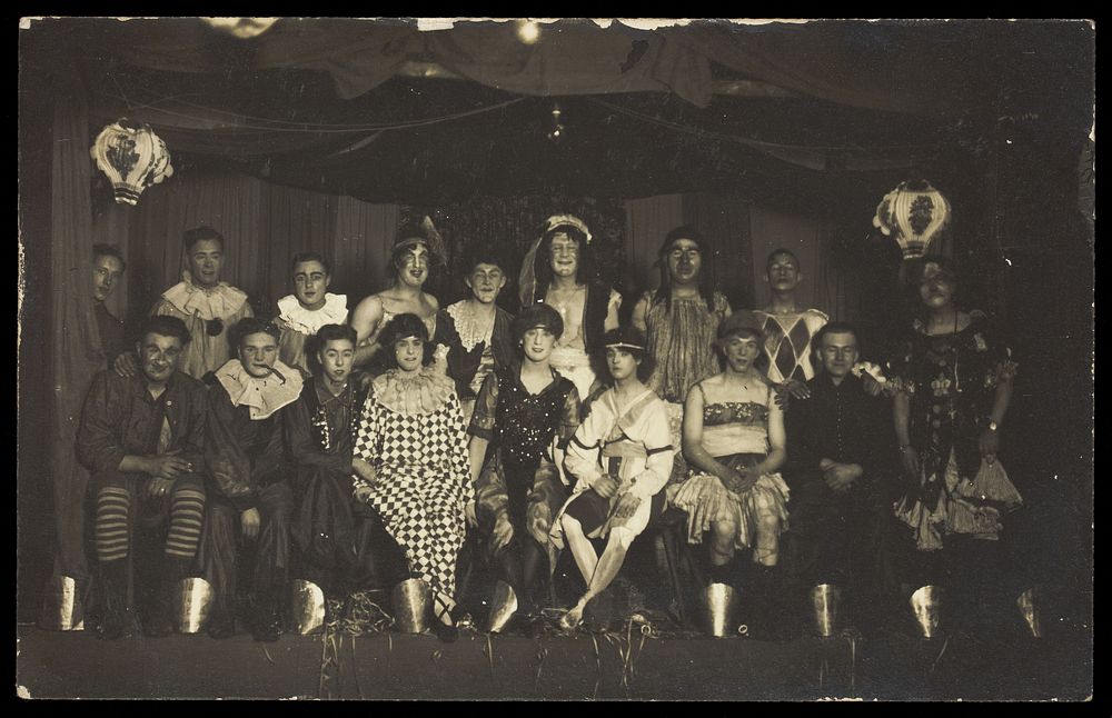 An ensemble cast of British soldiers, some in drag, pose on stage. Photographic postcard, 1919.