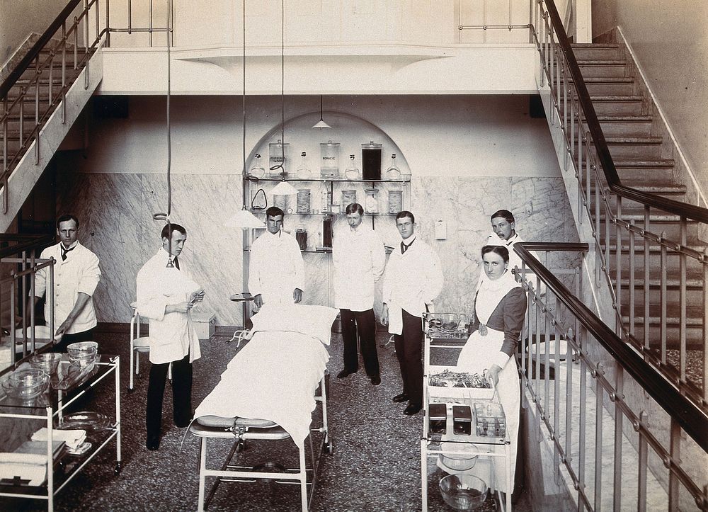 University College Hospital: medical staff in an operating theatre which has stairs leading up on either side. Photograph.