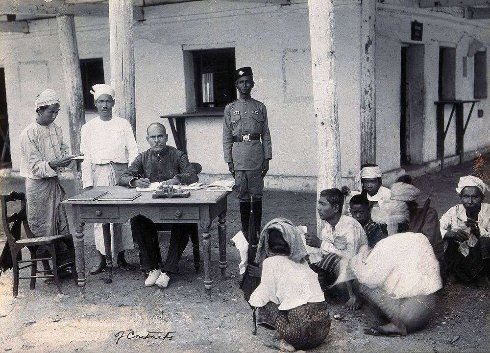 A man sitting at a table examining passports, during a plague epidemic in Mandalay. Photograph, 1906.