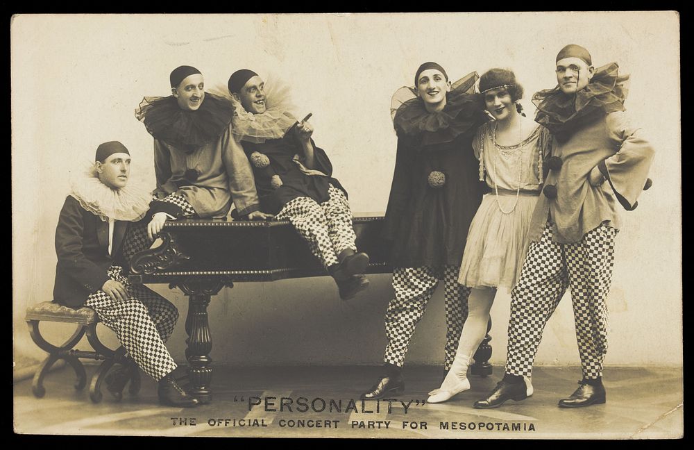 Soldiers, one in drag, performing in the concert party for Mesopotamia, posing around a piano. Photographic postcard by Hana…