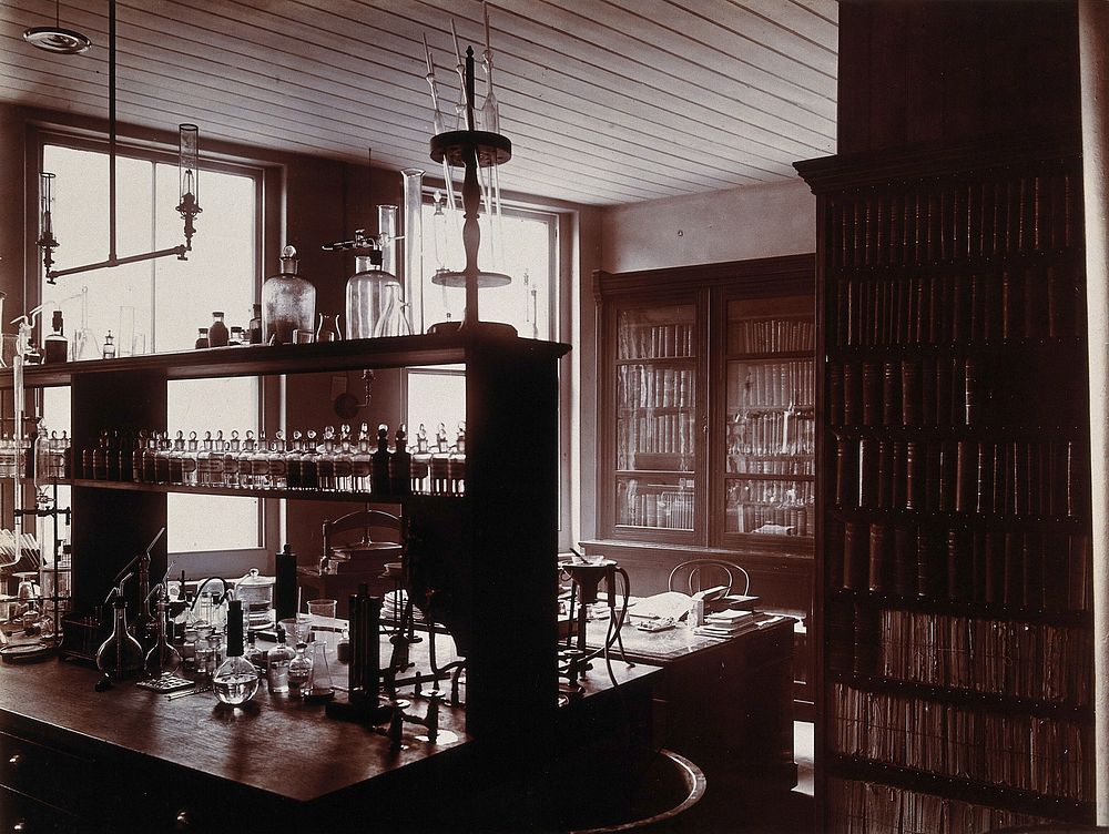The interior of a pharmaceutical or chemical laboratory with a bench in the centre and books and papers on shelves around…
