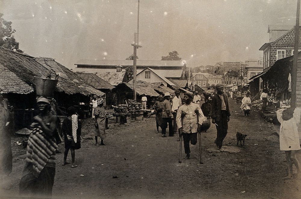 Freetown, Sierra Leone: local people, including an amputee on crutches, are shown walking along one of the principal…