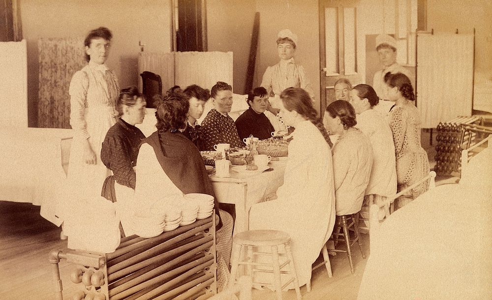 Bellevue Hospital, New York City: women patients (mentally ill) having a meal in a ward, with three nurses. Photograph.