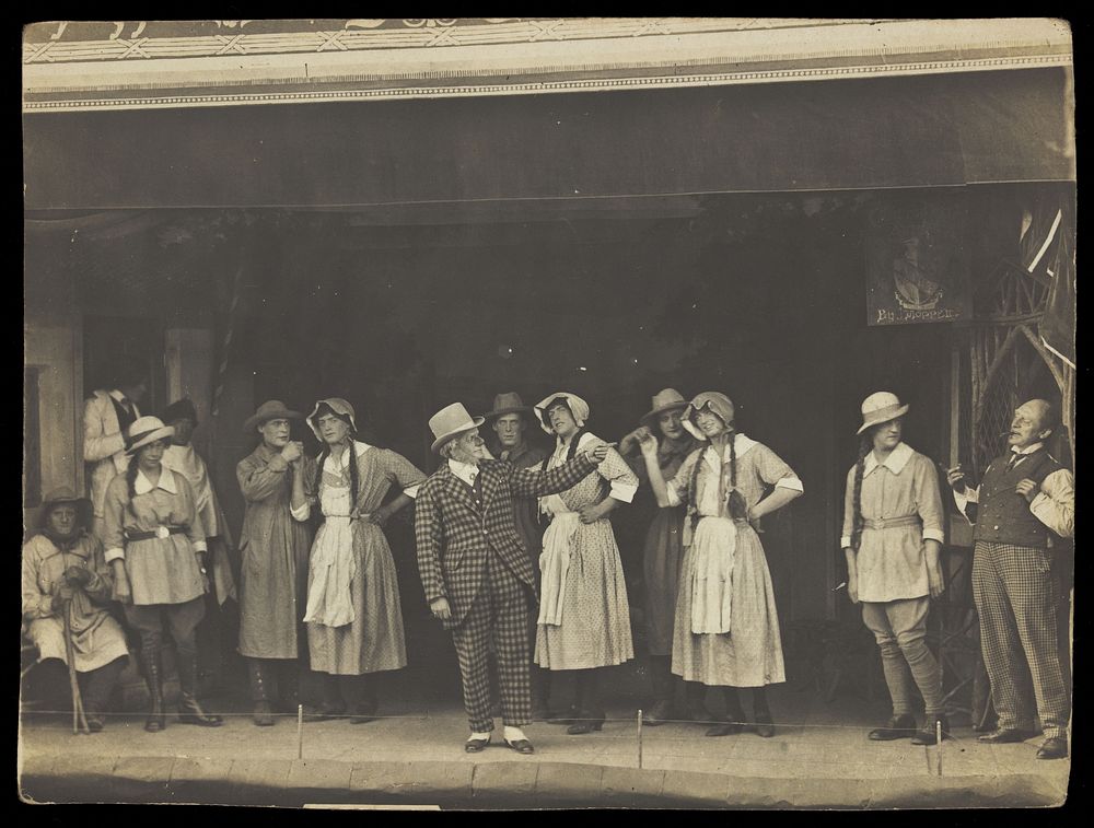 Sailors, some in drag, stand on stage performing a scene. Photographic postcard, 191-.