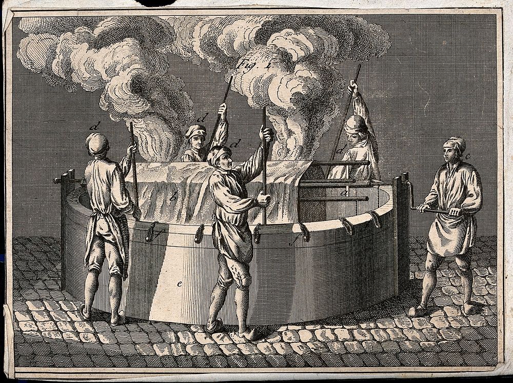 A large sheet is hanging over a series of rods suspended over a large steaming vat, one man turns a handle and others are…