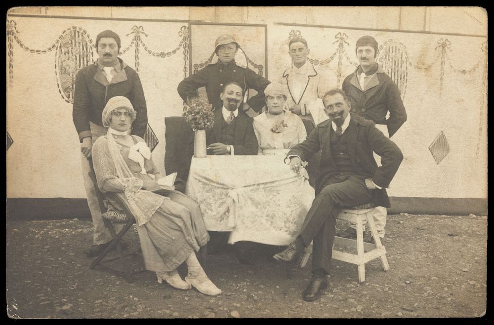German soldiers, some in drag, pose round a table at a concert party. Photographic postcard, 191-.