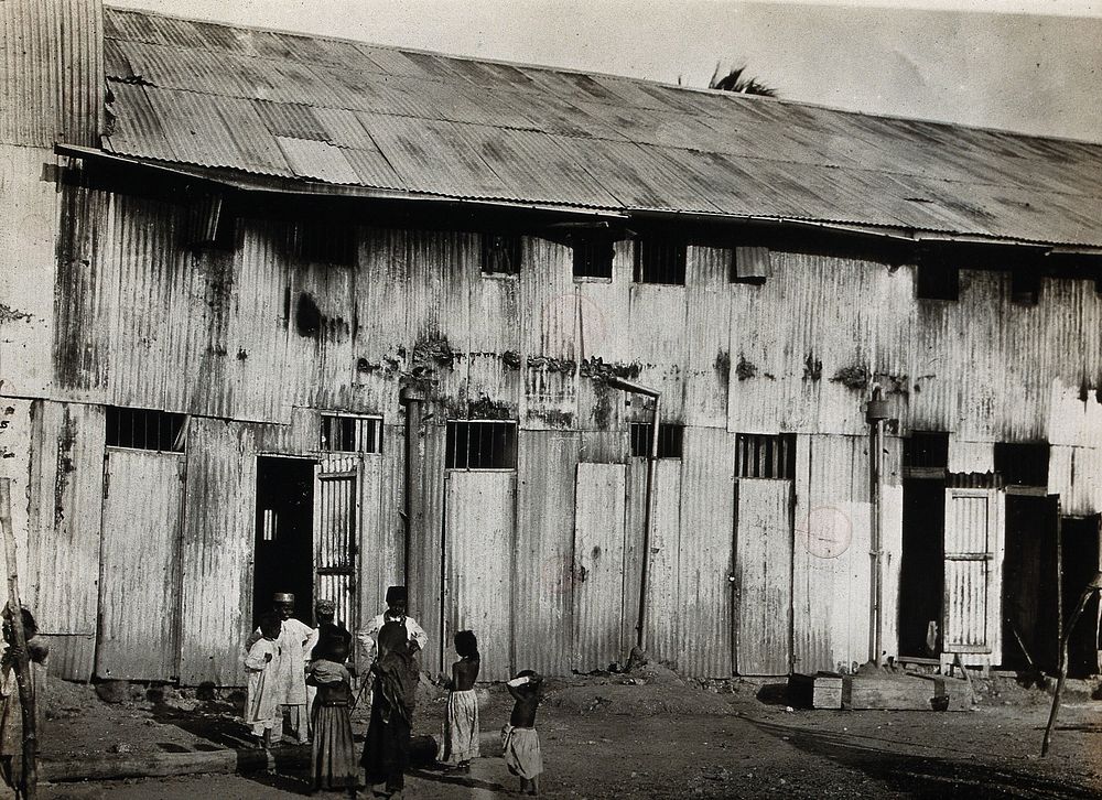 North Africa : institutional dwellings (possibly an orphanage) constructed of corrugated metal, with children standing in…