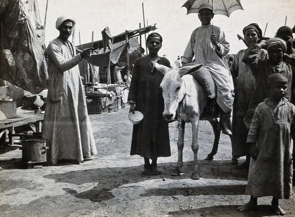 Tel-el-Kebir, Egypt: Egyptian men and children in a market;a boy on a donkey holding a parasol. Photograph, 1905/1920 .