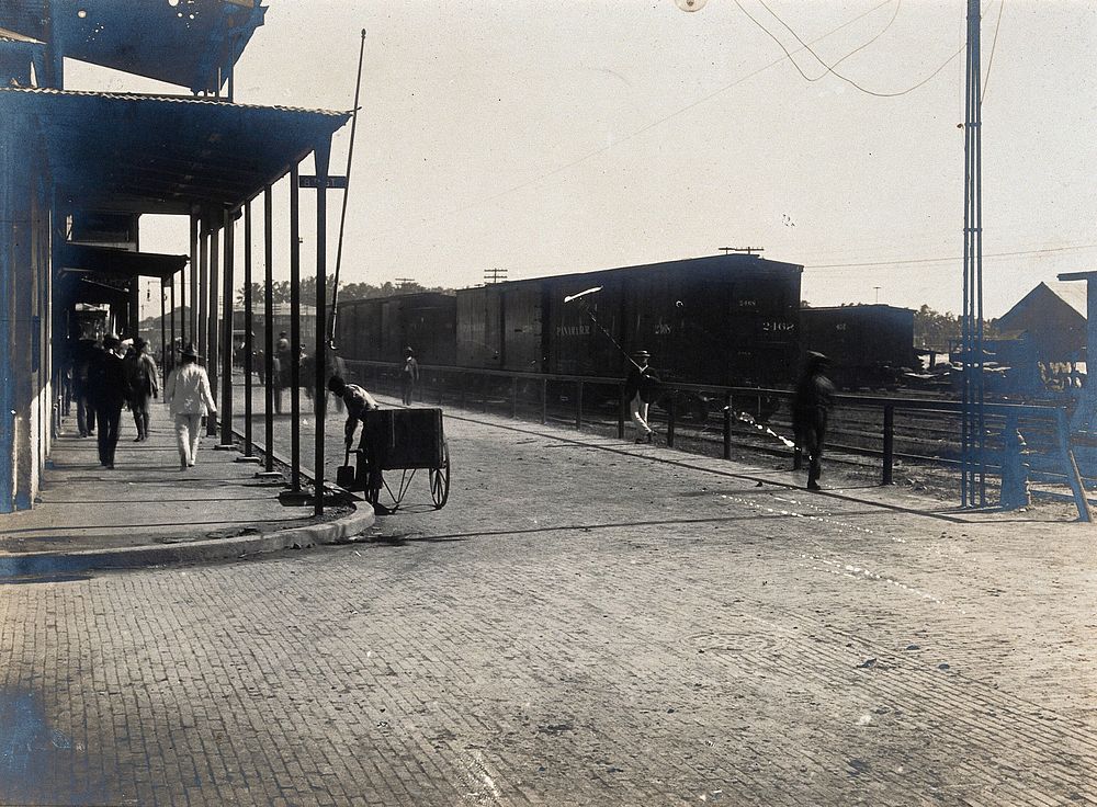 Colón, Panama: newly paved street junction with pedestrians, carriages and train carriages. Photograph, 1906.