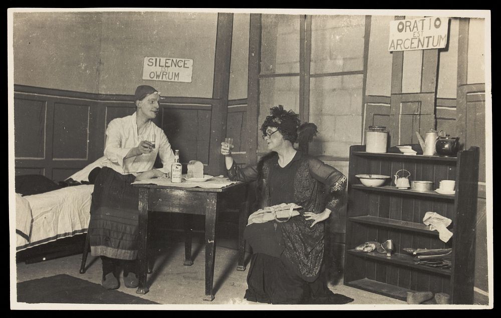 Two amateur actors, both in drag, having a drink on stage. Photographic postcard, ca. 1918.