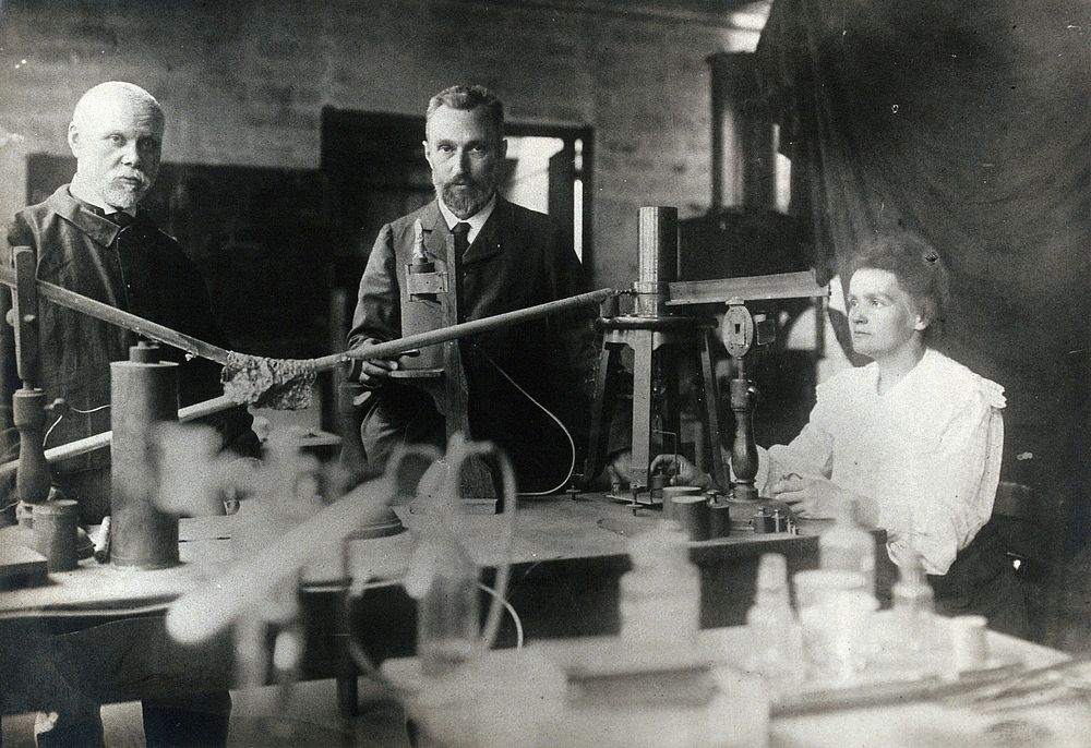 Marie and Pierre Curie (centre) with a man, using equipment in their laboratory, Paris. Photograph, ca. 1900.