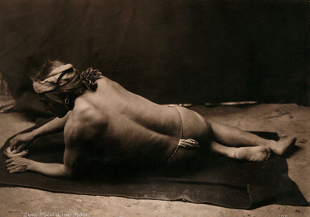 Zuni medicine man, New Mexico: reclining on a blanket wearing only a loin cloth, showing his back and his face in profile.…