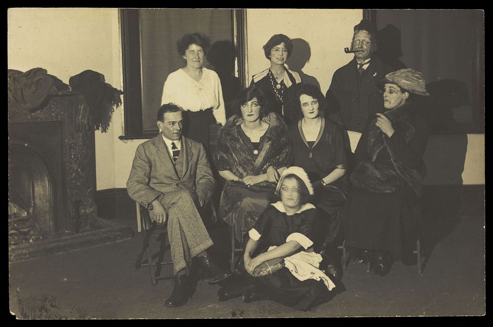 Amateur actors, some in drag, gather for a group portrait, in a room with a fireplace. Photographic postcard, 192-.