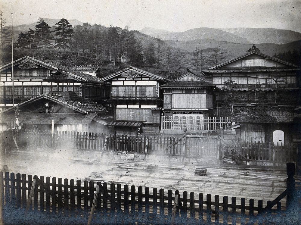 Japanese thermal baths, built outdoors behind wooden fences. Photograph.