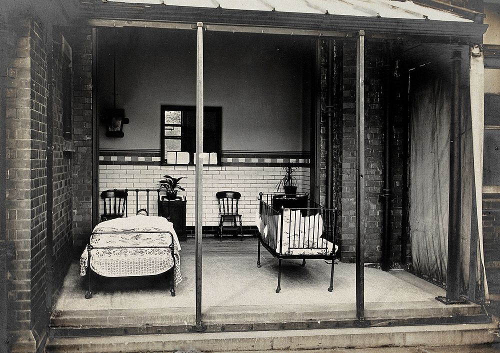 Nottingham: a verandah open to the air with a bed and a cot, each containing a child being treated for acute illness.…