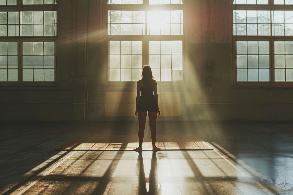 A woman poses for yoga in an gym backlighting sunlight standing.