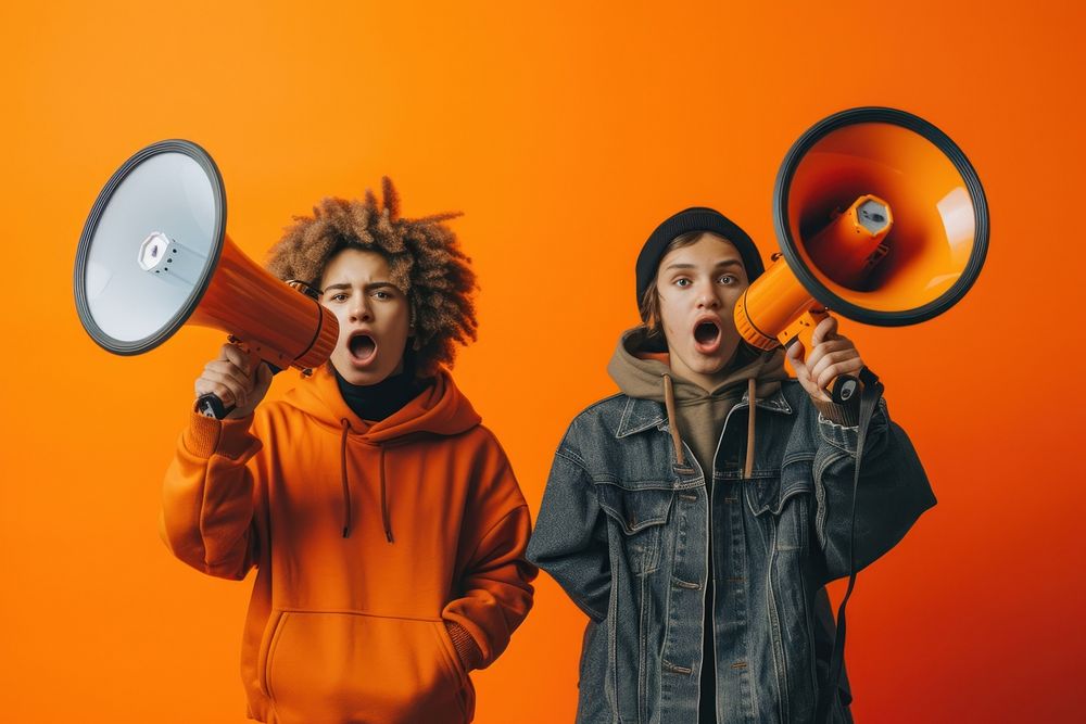 Two people holding megaphones while holding large signs on an orange background shouting adult togetherness.