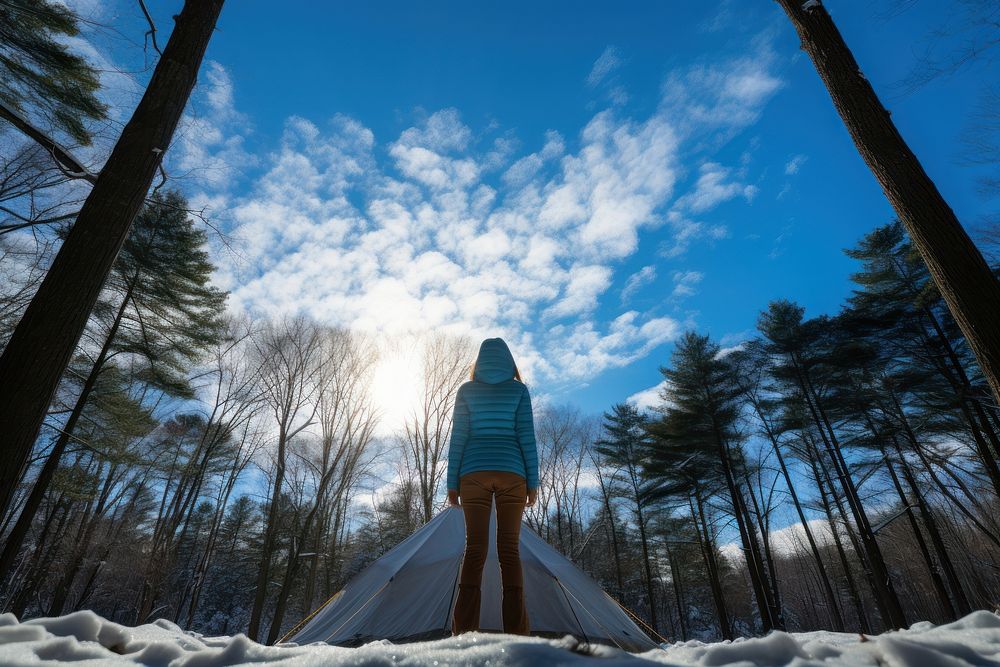 Woman standing in front of tent forest snow sky.