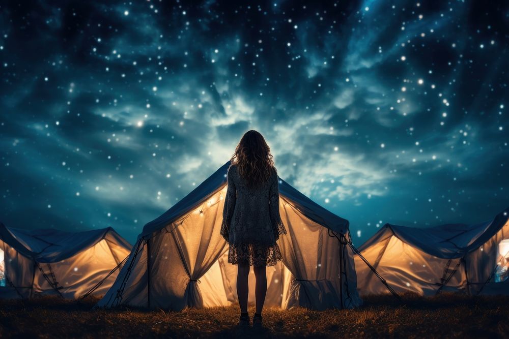 Woman standing in front of tent night outdoors camping.
