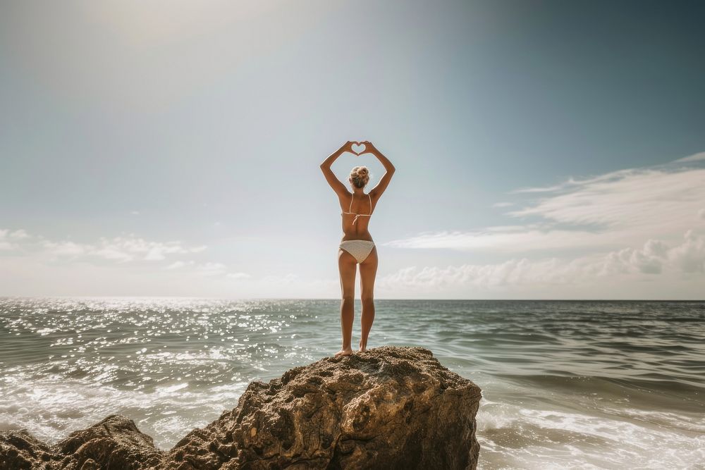 Woman standing on a rock at the beach outdoors vacation swimwear.