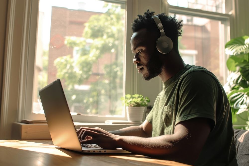 Black man typing on his laptop headphones computer sitting.