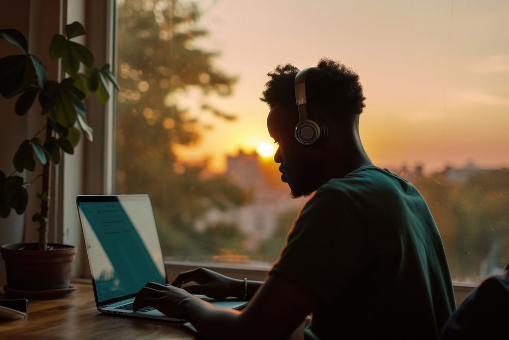 Black man typing on laptop headphones computer window.