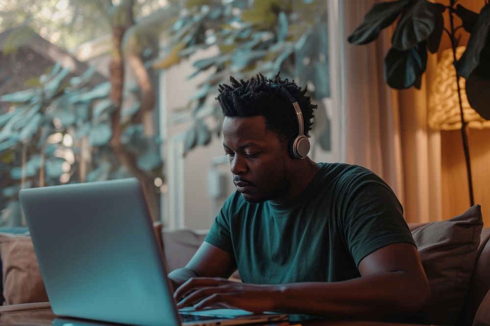 Black man typing on his laptop headphones computer concentration.