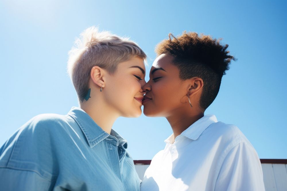 Lesbian couple kissing outdoors sunny blue.