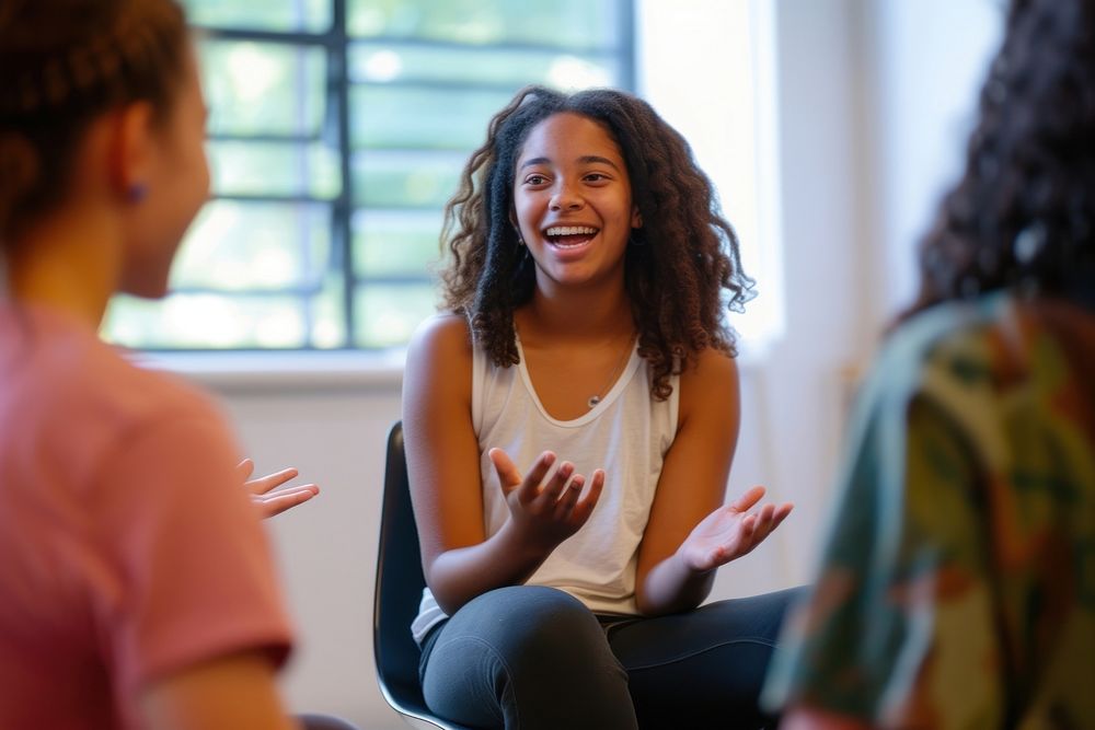 Girl seated on chair with other teens conversation therapy smile.